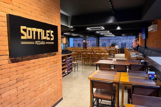 Mesas e cadeiras de madeira ao lado da parede de tijolinho com a placa Sottile's